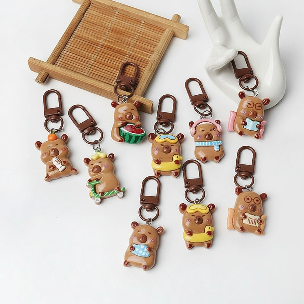 Set of 6 3D resin capybara bag charms lined up, featuring designs of capybaras reading, wearing a scarf, riding a scooter, eating watermelon, swimming with a floatie, and holding a fish.