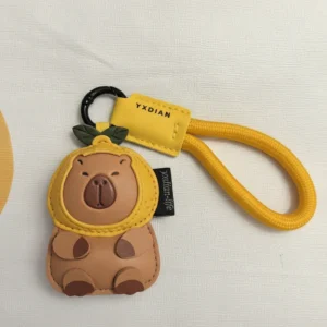 Close-up of a cute faux leather capybara keychain wearing a yellow lemon hood with a matching yellow rope strap and black metal clasp.