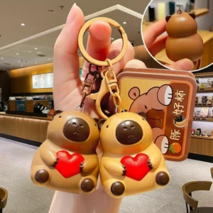 Two cute PVC capybara keychains in light and dark brown sitting and holding red light-up hearts with gold alloy clasps.