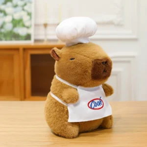 A cute brown capybara plush toy standing on a table wearing a white chef hat and an apron that says Cook.