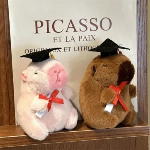 A brown and a pink capybara plush keychain sitting side by side, both wearing black graduation caps and holding diplomas with red ribbons.