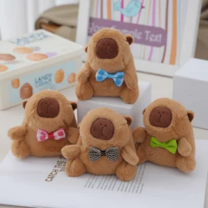 Four sitting capybara plush keychains arranged together, each wearing a different colored bow tie (pink, blue, brown, green).