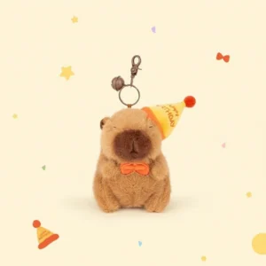 Front view of a sitting capybara plush toy wearing a yellow "Happy Birthday" cone hat and orange bow tie.