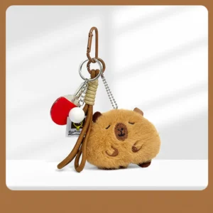 A round, fuzzy brown capybara plush keychain with closed eyes, featuring a bronze clip and a miniature ping pong paddle accessory.