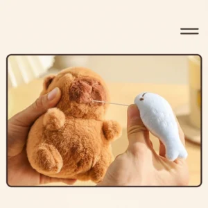 A 12cm interactive capybara plush keychain holding a Sacabambaspis fish, shown hanging from a bag with a pull-string mechanism that makes it shake.