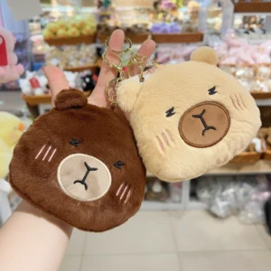 Fuzzy plush capybara head coin purses in dark brown and beige, featuring embroidered sleeping faces and gold keychain clips.